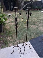 Full view of both wrought iron candle stands showing height and base structure on outdoor patio area with lawn background.