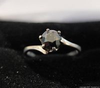 Front close-up of sterling silver ring with round black diamond in six-prong setting on black fabric background.