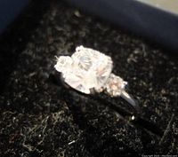 Close-up photo of ring showing large cushion-cut cubic zirconia center stone with two smaller round stones on the sides.