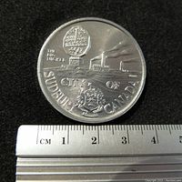 Close-up image of the Big Nickel side of the medallion showing embossed monument and inscription with a ruler for scale.