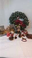 Photo showing full Christmas wreath, red flower accents, pinecones, metal stocking holder with 'Merry' lettering, snow globe, wooden rocking horse ornaments, and a red candle for scale