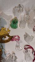 Clear crystal ornaments shaped as angels, birds, bells, and hands with red ribbons and wire hangers displayed on white background