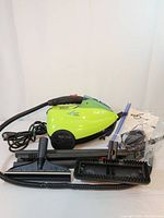 Side view of the Euro Steam Green Pro steamer unit with hose, wand, cleaning attachments, user manual, and power cord all laid out on floor.