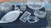 Top view showing all glass and crystal serving dishware including fish-shaped plates, butter dish, footed dish, large bowl with lid and four other dishes.