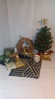 Gold-themed Christmas decorations including a small artificial tree with red berries and gold star topper, grapevine wreath with gold reindeer, navy and gold table runner, and gold vinyl tablecloth.