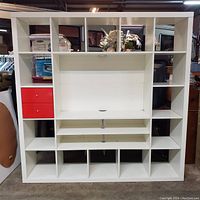 Front view of white Ikea Expedit (Kallax) TV storage unit showing central open space for TV, two red drawers on left, and multiple cubbies around sides