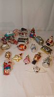 Photo showing overview of twenty plus mercury glass Christmas ornaments laid out on white background. Includes Santa, Nutcracker, football, vehicle with tree, and other holiday figures and objects