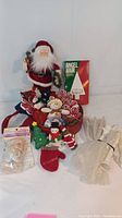 Photo showing Santa figure, box of Angel Hair, Christmas-themed stuffed ornaments, and porcelain Santa head bowl grouped on table.