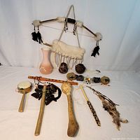 Full display showing three pottery pieces, wooden flute, three rattles, handheld drum, bow with two arrows in fur sheath.