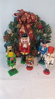 View showing all five nutcracker figurines displayed in front of the decorated wreath, capturing varied sizes and colorful detailing of each figure and the wreath's holiday decorations.