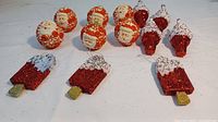 Photo shows red glittered ice cream bar ornaments with white frosting and gold sticks, along with spherical Santa face ball ornaments with red and white details.