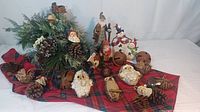Full view of rustic Christmas decorated metal sleigh with pinecone Santa ornaments, owl ornaments, large metal bells and wooden Santa and snowman figures arranged on red plaid fabric.