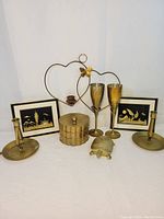 Full view of the lot including framed straw pictures, brass candle holders, lidded container, turtle figurine, and champagne flutes.