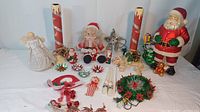 Wide shot of the vintage Christmas decor assortment including angel tree topper, candles, various Santa figures, and ornaments spread on a white surface.