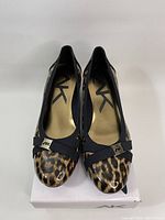 Top view of the pair of Anne Klein wedge shoes showing leopard print toe with black crisscross straps and metal AK logo accents.