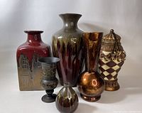 Front view of 7 decorative vases and urn in various shapes, colors, and materials