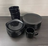Grouped view of the black Gibson stoneware set including plates, square saucers, bowls stacked, and a single mug.