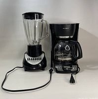 Black Oster blender with clear glass jar and black lid, multiple speed buttons on silver base; black Mr. Coffee drip coffee maker with glass carafe and black handle, water reservoir lid and front control buttons