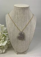 Full front view of heart pendant necklace on neutral fabric bust with white flowers on the side