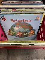 Photo of vinyl records in red crate with The Care Bears 'Off to See the World' album cover visible on front.