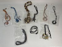 Full view of 8 necklace and earring sets and 2 bracelets in plastic packaging, laid flat on white surface.