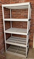 Front view of the 4-tier plastic storage shelving unit placed against a brick wall, showing all shelf levels and black corner connectors.