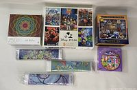 Top-down photo showing all puzzles and three Diamond Dotz kits: 5 Disney Pixar puzzles, Cat Around the World Dobble puzzle, a 750-piece abstract art puzzle, the circular Disney Princess puzzle, and three wrapped Diamond Dotz kits.