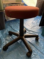 Side view of burgundy rolling task chair with round cushion and black base with casters.