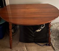 Round wooden table with two drop leaves lowered, showing half-circle top with four turned legs.