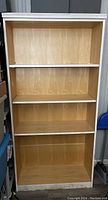 Front view of the tall wooden bookcase showing four shelves inside, natural wood interior with white trim at edges.