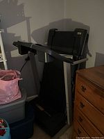 Folded treadmill in corner next to dresser and storage bins