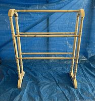 Front view of vintage white wooden quilt rack displayed on blue background, showing full structure including spindle sides and three horizontal bars.