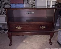 Front view of the wooden TV stand showing the open shelf with cable hole, drawer with brass handles, and curved legs.