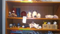 Shelf with various art pieces including ceramic eggs, dolphin sculpture, shells, wooden blocks with figurines and pill box