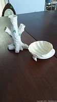 Photo of Belleek white porcelain tree trunk style vase with three openings and green shamrock decoration, next to small shell dish