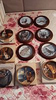 Photo showing all eleven plates arranged on a floral fabric surface; includes mixtures of human Norman Rockwell art and wildlife scenes.