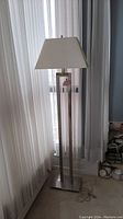 Full view of the metal floor lamp with white rectangular shade standing near a window with curtains.