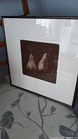 Framed print of two pears with white mat and dark wood frame, placed on a chair.