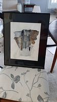Framed mixed media art showing full artwork, black frame, and reflective glass surface.