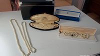 Four pearl necklaces and one pair of pearl screw-back earrings displayed with cases.