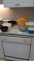 Yellow and white plastic salad spinner with lid, three Pyrex mixing bowls in black, white, and yellow, plus a blue bowl and clear glass Pyrex bowls seen on kitchen counter.