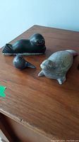 Three soapstone animal figures on a wooden surface: seal, bird, and turtle with visible surfaces and dimensions.
