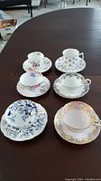 Six teacup and saucer sets arranged on a table showing their design patterns.