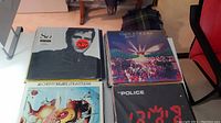 Nine vinyl LP record albums on a table, titles visible include Supertramp Paris, Dire Straits Alchemy Live, The Police