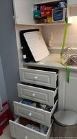 Photo showing kitchen drawers with utensils and a nearby kitchen waste can