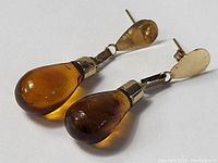 Pair of 10K gold earrings with amber teardrop pendants lying flat to show the amber tones and gold fittings.