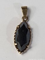 Front view of the gold pendant showing the faceted black onyx stone in a prong setting and bail for chain attachment.