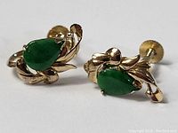 Close-up front and side views of the pair of vintage 14K gold earrings with teardrop green jade stones and decorative gold leaf accents, showing twist-on screw back closures.