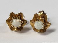 Front view of the pair of 14k gold earrings with round white opal stones set in a scalloped petal design.