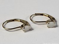 Pair of 14K gold earrings each set with an oval opal stone in prong settings, vintage style, with hinged lever-back clasp.